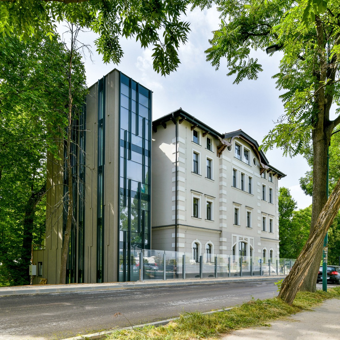 Ugao historijske zgrade s modernom staklenom dogradnjom, okružena zelenilom