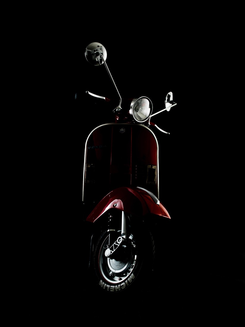 Prednji dio vintage Vespa skutera fotografiran u dramatičnom niskom osvjetljenju na crnoj pozadini