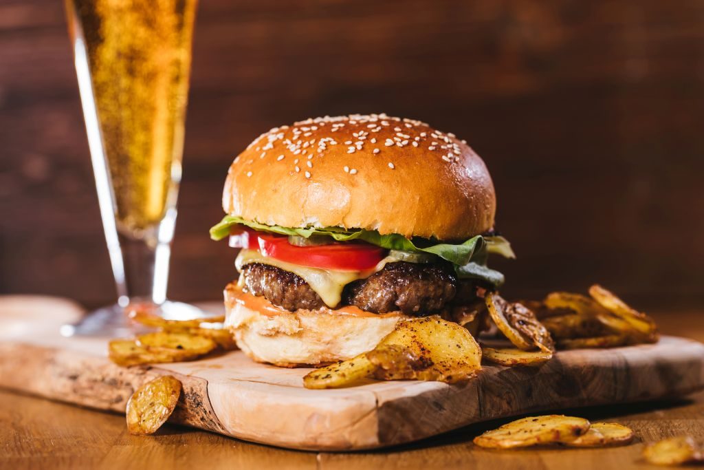 Gurmanski burger sa pečenim krompirićima i čašom piva na drvenoj dasci